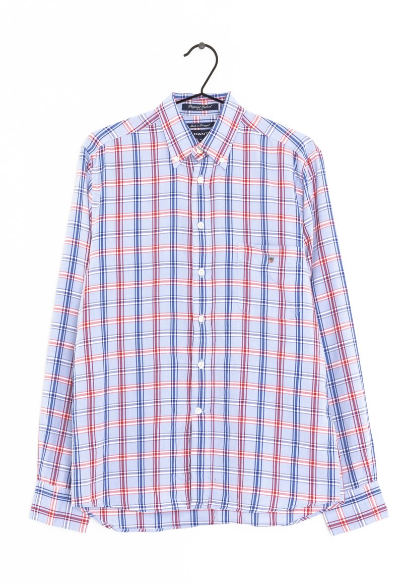 Camicia a quadri con righe blu, rosse e bianche, maniche lunghe, colletto a bottoni e taschino sul lato sinistro del petto. Il tessuto sembra leggero.