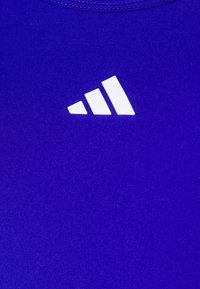 Ljubičasti sportski majica bez rukava od glatkog materijala, s bijelim logotipom u obliku tri pruge na području prsa.