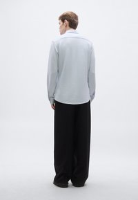 Svetlomodrá košeľa s dlhými rukávmi a golierom a čierne široké nohavice, pohľad zozadu na jednobielom pozadí.