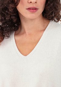 Pull en tricot gris clair avec un col en V, présentant une texture douce et un détail de couture subtil autour de l'encolure.