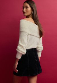 White off-the-shoulder fuzzy sweater with rolled sleeves paired with a black denim mini skirt featuring visible stitching and a zip closure.