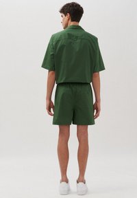 Camicia verde a maniche corte e pantaloni corti abbinati realizzati in tessuto leggero, con una vestibilità rilassata e un sottile dettaglio sulla tasca posteriore. Sneakers bianche.