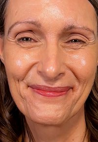 Nærbilde av en kvinnes ansikt, med glatt hud med lett tekstur, lys sminke på leppene, varme undertoner og milde smilelinjer.