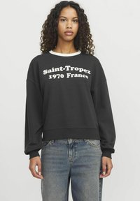 Černá mikina s bílým nápisem "Saint-Tropez 1970 Francie", kulatý výstřih, žebrované manžety a volný střih. Nosit s světle modrými džínami.