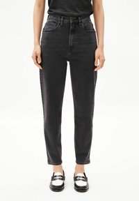 Jean en denim noir taille haute avec une coupe fuselée, poches avant et légère décoloration. Associé à des mocassins noirs et blancs.