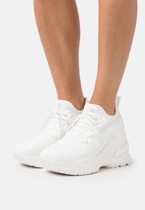 Zapatillas deportivas blancas con parte superior de malla texturizada, suela de goma gruesa y cordones en la parte delantera. Presenta un cuello acolchado y acentos mínimos.