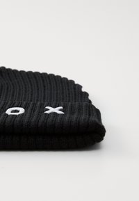 Bonnet en tricot noir à côtes avec un ourlet replié. Présente des lettres blanches brodées "o" et "x" à l'avant. Texture douce et finition lisse.