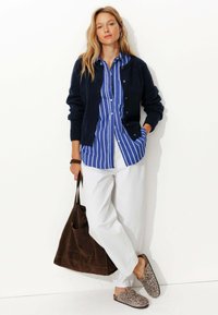 Cardigan marine sur une chemise rayée bleu et blanc, pantalons blancs, sac en suède marron, et chaussures à enfiler à imprimé léopard.