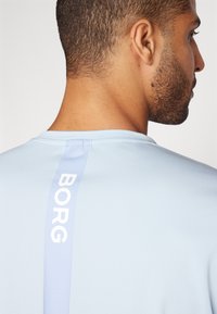 Camisa deportiva de manga corta de color azul claro con una textura suave, que presenta un logo vertical en blanco "BORG" a lo largo de la costura trasera.