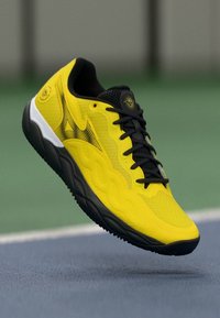 Adidași galbeni pentru sport, cu un superior din plasă, accente negre și o talpă bine amortizată, având un logo distinctiv și un design texturat.