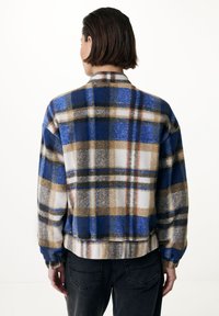 Modrá, hnědá a bílá kostkovaná flanelová košile s uvolněným střihem, dlouhými rukávy a mírně zkráceným lemem, s jemnou texturou.