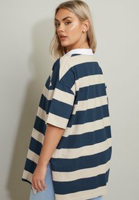 Marinblå och krämfärgad randig t-shirt med krage, korta ärmar och avslappnad passform. Mjuk tyg, sidoflikar och en något längre bakdel.