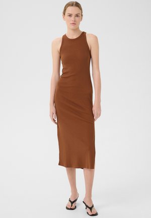 Vestido midi marrón de canalé con escote redondeado y diseño ajustado. Llevado con chanclas negras, con una textura de tela suave y elástica.