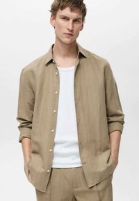 Beige stribet button-up skjorte lavet af letvægtsstof, med en afslappet pasform og ærmer der kan rulles op, over en hvid t-shirt.
