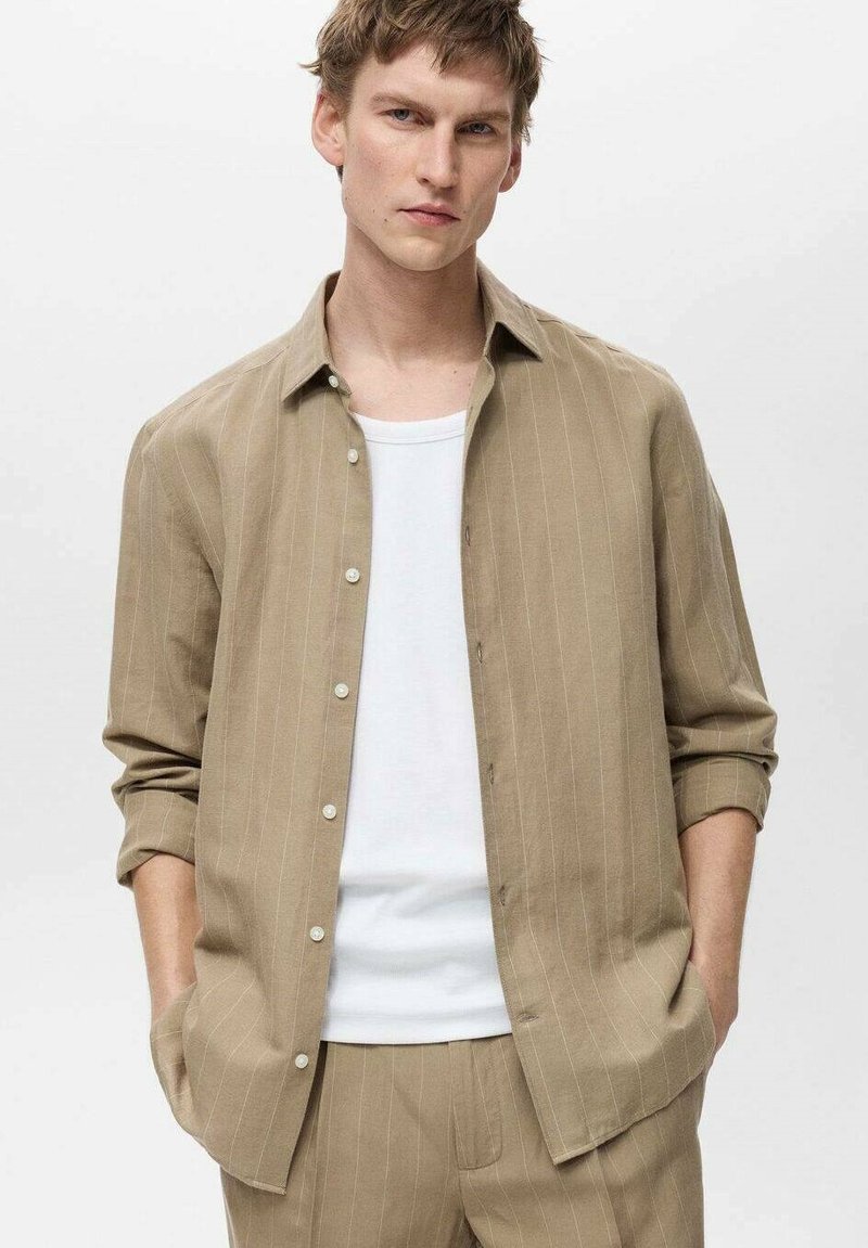 Beige stribet button-up skjorte lavet af letvægtsstof, med en afslappet pasform og ærmer der kan rulles op, over en hvid t-shirt.