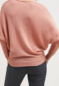 Maglione oversize rosa a maglia con silhouette ampia e polsini a coste, caratterizzato da una consistenza morbida e un collo leggermente alto.