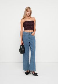 Burgundy floral-patterned crop top, high-waisted blue denim wide-leg jeans, black heeled shoes, and a small black handbag.