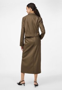 Veste marron ajustée avec une coupe courte, jupe longue assortie et sandales à talons noires. Le tissu est lisse avec un léger éclat.