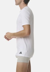 White short-sleeve t-shirt made of soft fabric, featuring a round neckline and a black Adidas logo at the lower left hem.