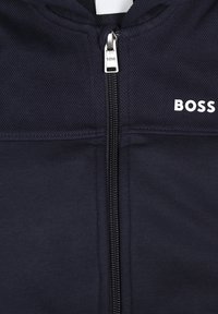 Hoodie zippé bleu marine avec une fermeture éclair argentée, un panneau supérieur texturé et un logo "BOSS" blanc à l'avant. Fabriqué en matériau doux et flexible.