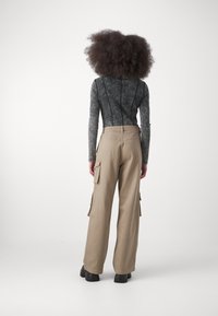 Dlouhý šedý top s texturovaným vzorem a černým prošíváním, kombinovaný s béžovými cargo kalhotami s vysokým pasem a bočními kapsami.