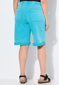 Shorts en denim aquamarine avec des ourlets roulés, une taille élastique et deux poches arrière. Portés avec des sandales noires au design texturé.
