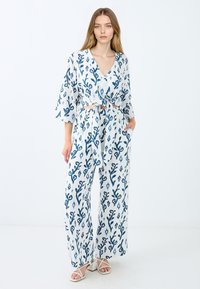 Weiß-blau gemustertes Zweiteiler-Outfit mit weitem Bein und einem geknoteten, kurz geschnittenen Oberteil. Hergestellt aus leichtem Stoff mit floralem Design.