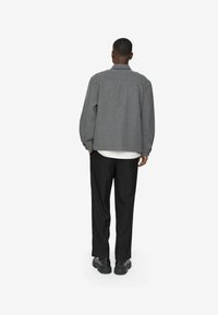 Jachetă din lână gri cu amestec, cu guler de cămașă, umeri lăsați și o croială relaxată, asociată cu pantaloni negri stilați și încălțăminte masivă neagră.