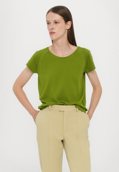 Green short-sleeve T-shirt in a soft texture with a round neckline, paired with fitted beige trousers featuring a slim cut and front crease.