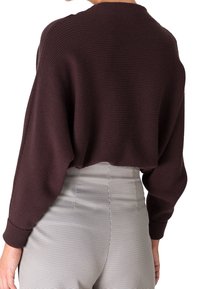 Pull court marron en tissu côtelé texturé, manches longues et col rond. Associé à un pantalon taille haute à carreaux.