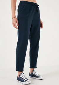 Námořnické modré joggingové kalhoty z lehkého materiálu s elastickým pasem, zúženými nohavicemi a manžetami, spárované s bílými teniskami.