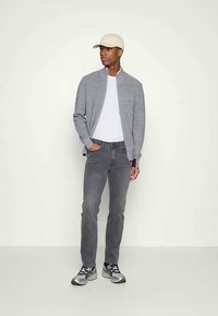 Gray lightweight cardigan over a white shirt, paired with gray jeans and black and yellow sneakers, finished with a beige cap.