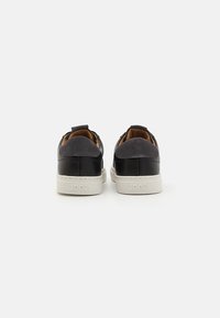 Svarte og grå lær sneakers med en hvit gummisåle, med en semsket detalj på hælen og en løkke for enkel påkledning.