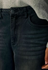Jeans in denim nero con chiusura a bottone, design a cinque tasche e sottili variazioni di texture nel tessuto.