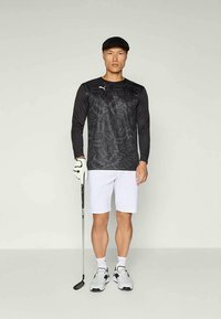 Fekete, hosszú ujjú sportpóló, texturált mintával, fehér rövidnadrággal, sportkesztyűvel és golfütővel. A fehér sportcipő tökéletesíti a megjelenést.