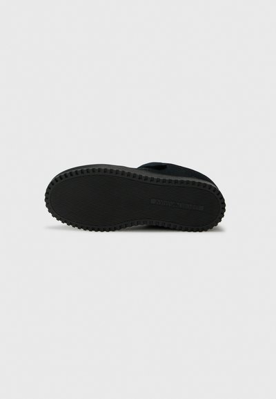 Black rubber shoe sole with textured tread pattern and embossed branding. Flat, round-shape design suitable for various footwear styles.