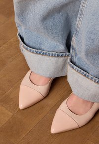 Scarpe in pelle rosa con punta a punta e taglio basso, abbinate a jeans di denim azzurro chiaro arrotolati con orlo sfilacciato e cuciture a contrasto.