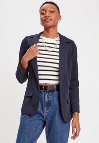 Navyblauwe blazer met een op maat gemaakt ontwerp, twee voorzakken, gedragen over een zwart-wit gestreepte top, gecombineerd met hoge taille spijkerbroek.