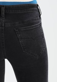 Vaqueros de mezclilla negra con un diseño ajustado, que presentan un bolsillo trasero con detalles bordados y un acabado texturizado. Silueta estrecha, desgaste mínimo.