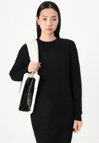Vestido de punto acanalado negro combinado con un bolso de mano blanco y esponjoso con superficie brillante negra y forma rectangular.