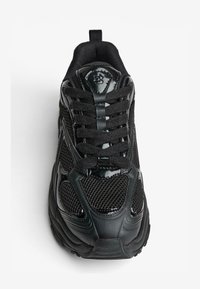 Čierna športová obuv z kombinácie sieťoviny a kože. Má zaoblenú špičku, polstrovaný jazyk a textúrovanú podrážku. Obsahuje čierne šnúrky a detaily loga.