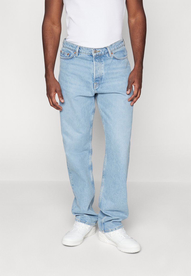 Lyseblå denimjeans med lige ben, fem lomme-design og subtil slitage. Båret med hvide sneakers og en tætsiddende tanktop.
