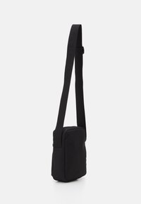 Black crossbody bag made of durable fabric, rectangular shape, featuring a adjustable strap and a zip closure. Smooth texture, minimalist design.
