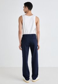 Navy trousers with a straight cut, featuring two back pockets and a waistband, paired with a white sleeveless top. Smooth fabric texture.