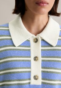 Sweter polo z białym prążkowanym kołnierzykiem i czterema guzikami. Charakteryzuje się niebieskimi i zielonymi paskami na teksturowanym tle.