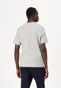 Tricou gri cu mânecă scurtă, confecționat dintr-un material mixt de bumbac, având un guler clasic în formă de cerc și o croială lejeră, văzut din spate.