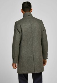 Grijze wollen jas met hoge kraag, getailleerde pasvorm en een enkele split achter. Voorzien van knoopmanchetten en een logodetail op de kraag.