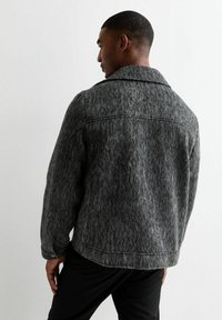 Chaqueta de lana gris con un cuello estructurado y mangas largas, que presenta un tejido texturizado y detalles de costura visibles en la parte posterior.