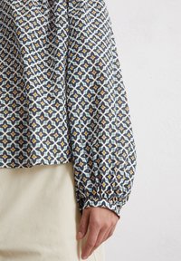 Langarmbluse aus leichtem Stoff mit einem geometrischen Muster in Marineblau, Weiß und Senfgelb. Mit gerafften Manschetten und einer lockeren Passform.