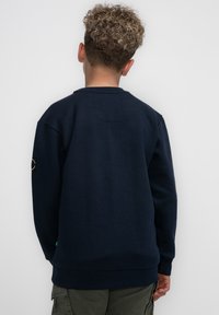 Felpa blu navy realizzata in tessuto morbido, con polsini e orlo a coste, caratterizzata da un collo rotondo e una patch logo sulla manica sinistra.